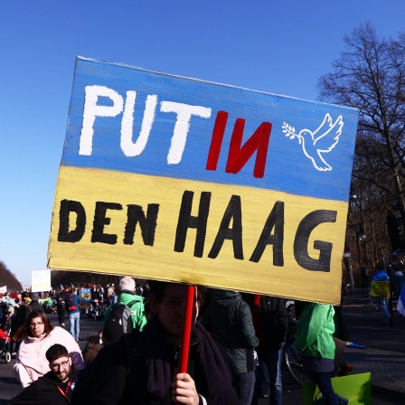 Ein Berliner Demonstrant hält ein Schild mit der Aufschrift &#034;Putin Den Haag&#034;