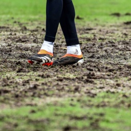 Füsse auf dem von Regen und Wetter stark zerstörten Fußballfeld.