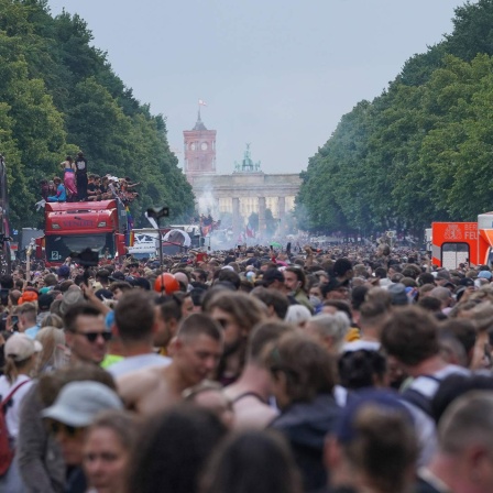 Die Techno-Parade "Rave the Planet" zieht im Juni 2022 durch Berlin - im Hintergrund sind Brandenburger Tor und Rotes Rathaus zu sehen. 