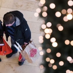 Zwei Menschen stehen in einem Einkaufszentrum und begutachten gegenseitig ihre Weihnachtseinkäufe.