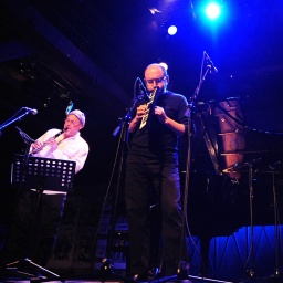 Drei Männer musizieren mit Musikinstrumenten auf einer Bühne.