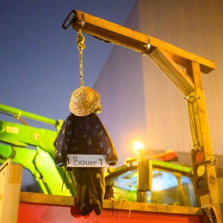 Eine kleine Bauernpuppe hängt an einem Galgen mit Ampel-Symbol bei einer Demonstration von Landwirten (Bild: picture alliance/dpa/Julian Stratenschulte)