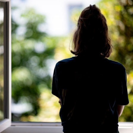 Eine Frau steht in ihrer Wohnung an einem Fenster.