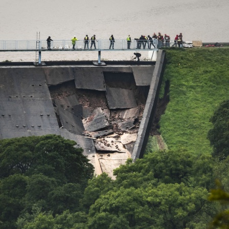Großbritannien, Whaley Bridge: Menschen bilden über dem beschädigter Teil an einem Staudamm am Toddbrook Reservoir eine Menschenkette, um Sandsäcke auszulegen