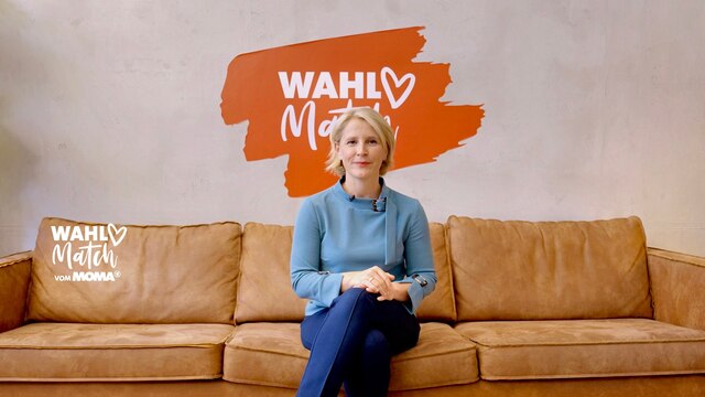 Moderatorin Susan Link sitzt mittig auf einer Ledercouch, im Hintergrund an der Wand ist ein orangenes Logo mit weißer Schrift "Wahl Match" zu sehen