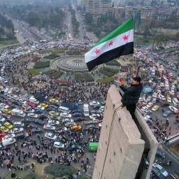 Ein Mann schwenkt die syrische Oppositionsflagge auf einem Denkmal auf dem zentralen Umayyad-Platz in Damaskus.