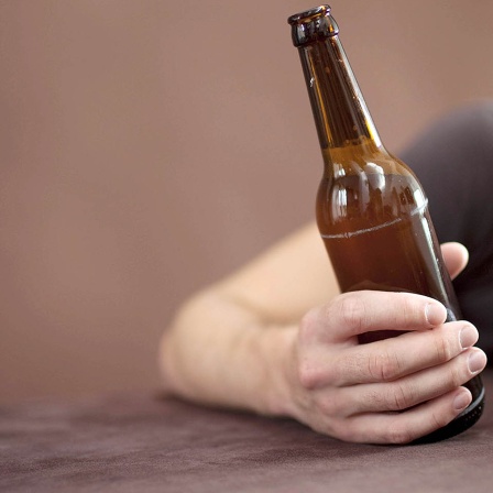 Betrunkener Mann schläft mit Bierflasche in der Hand.
