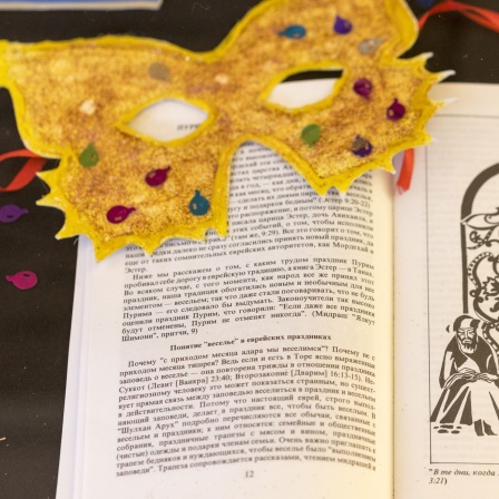 Eine Maske und Konfetti liegt auf Buch Ester, aus dem zu Purim traditionell vorgelesen wird liegt. Symbolbild