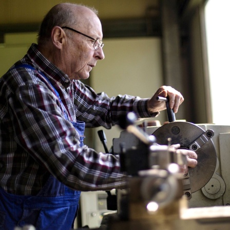 Ein älterer Herr arbeitet in einem mittelständischen Unternehmen für Maschinenbauteile an einer Drehmaschine.