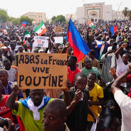 Menschen halten Plakate und Fahnen während sie an einem Marsch teilnehmen, zu dem Anhänger des Putschisten General Omar Tchiani im Niger aufgerufen haben.