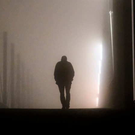 Ein Mann geht am frühen Morgen bei Nebel alleine über eine Brücke.