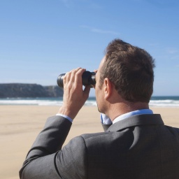 Ein Mann blickt mit einem Fernglas in die Ferne, während er am Strand steht