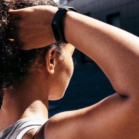 Eine Frau trägt einen Fitness-Tracker am Handgelenk und fährt sich während sie steht durch die Haare.