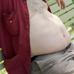 Ein Mann mit dickem Bauch sitz auf einer Bank.