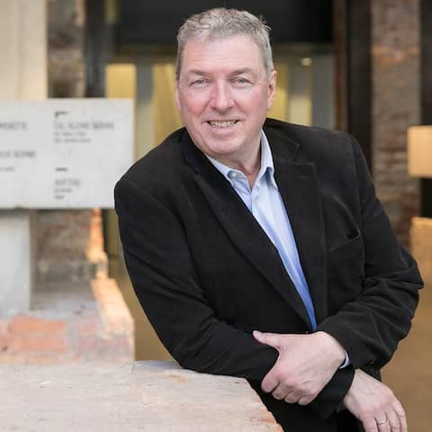 Wolfgang Schaller, Intendant der Staatsoperette Dresden, im Porträt, im Hintergrund undscharf Treppenhaus und Wegweiser der Staatsoperette