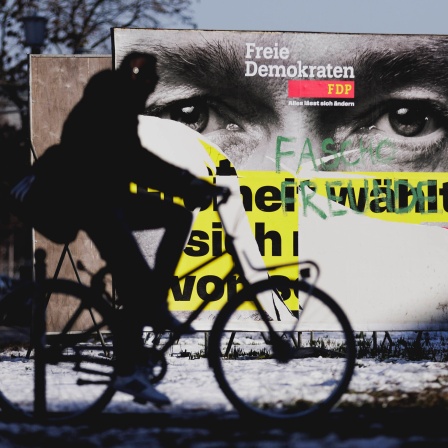 Radfahrer fährt an einem beschmierten Wahlplakat von der FDP mit Christian Lindner vorbei, Schnee auf Boden