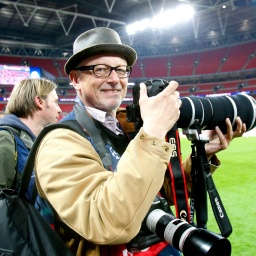 Der Sportfotograf Laci Perényi steht mit seiner Kamera auf einem Fußballfeld.