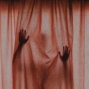 Eine Gestalt mit erhobenen Händen hinter einem verschlossenen roten Vorhang