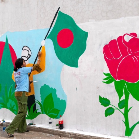 Graffiti auf einer Wand in Bangladesch: Eine Studentin malt einen Demonstranten, der eine Flagge von Bangladesch hält, aus einer Rose wächst eine Faust.