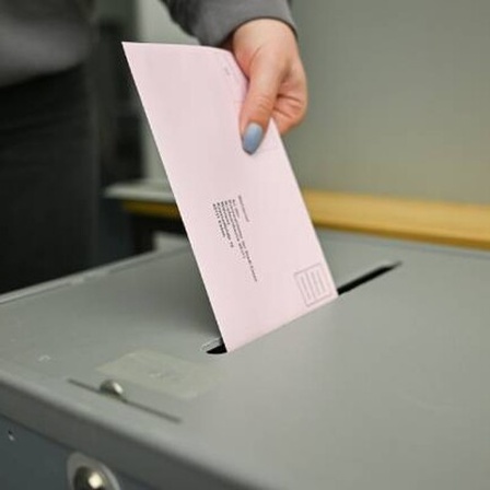 Eine Frau wirft den rosafarbenen Briefumschlag mit ihren Wahlunterlagen für die Bundestagswahl 2025 in die Wahlurne im Wahlamt in Essen.