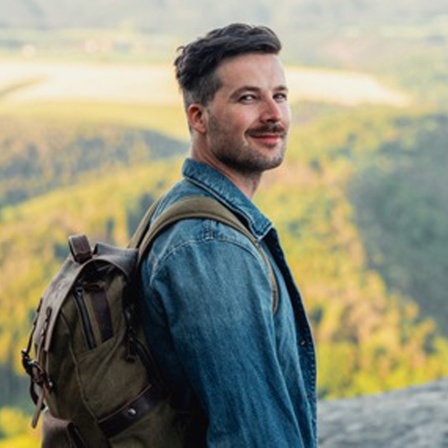 Simon Hegewald, Wander-Influencer, steht mit Rucksack auf einer Anhöhe. Im Hintergrund sind herbstlich bewaldete Hügel zu sehen. In SWR1 Leute beschreibt er seine unvergesslichen Reiseziele und verrät Tipps, was Wandern heute attraktiv macht. 