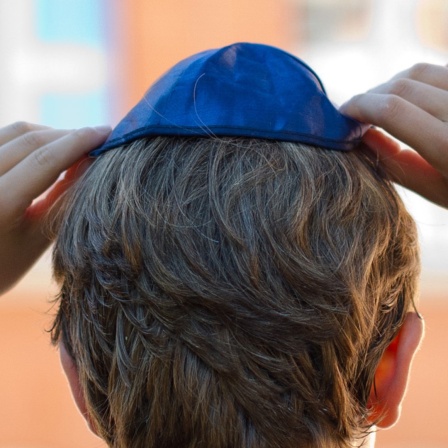 Ein Junge setzt sich eine Kippa auf den Kopf.