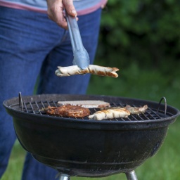 Mann am Grill mit Wurst in der Zange