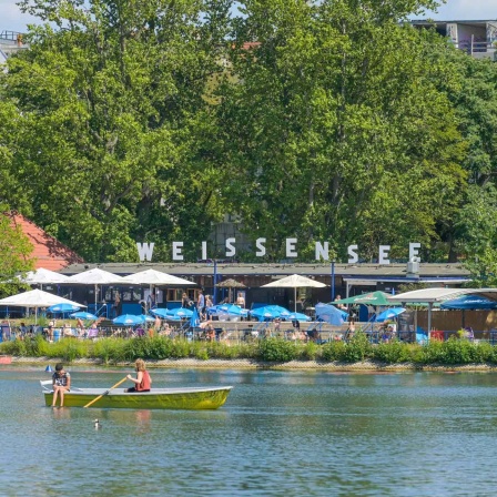 Ein Ruderboot fährt am Strandbad Weißensee vorbei.