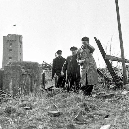 Drei Bewohner besichtigen am 1. März 1952 die völlig zerstörte Hauptstraße der Insel Helgoland.