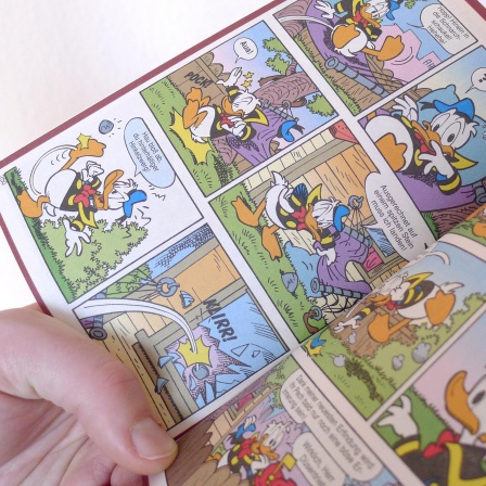 Eine Hand hält ein offenes Donald Duck Heft, ein LTB, "Lustiges Taschenbuch Comic".
