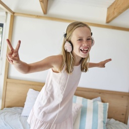 Mädchen tanzt mit Kopfhörern auf einem Bett