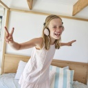 Mädchen tanzt mit Kopfhörern auf einem Bett
