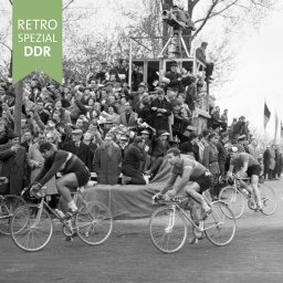 Radfahrer fahren vorbei an Tribüne mit Zuschauern und Kamerateam (Friedensfahrt 1962)