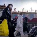 Peking: Reisende mit Mund-Nasen-Schutz gehen mit Koffern an dem Zentralbahnhof vorbei