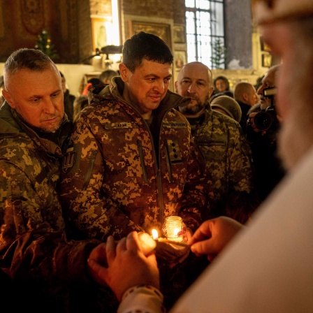 Ukrainische Soldaten erhalten von einem Priester das Friedenslicht von Bethlehem, während eines Weihnachtsgottesdienstes. 