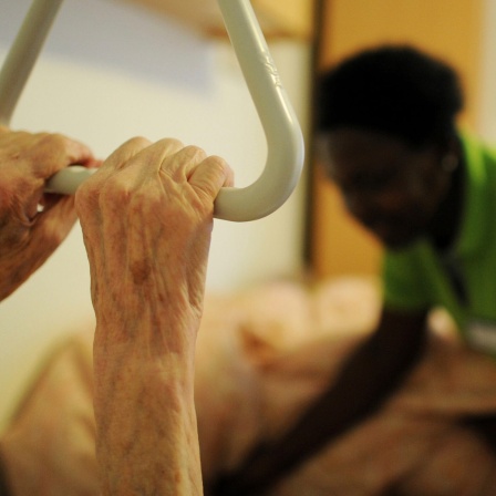 Eine Pflegehelferin hilft  in einem Seniorenzentrum einer Pflegehausbewohnerin, sich hinzulegen.