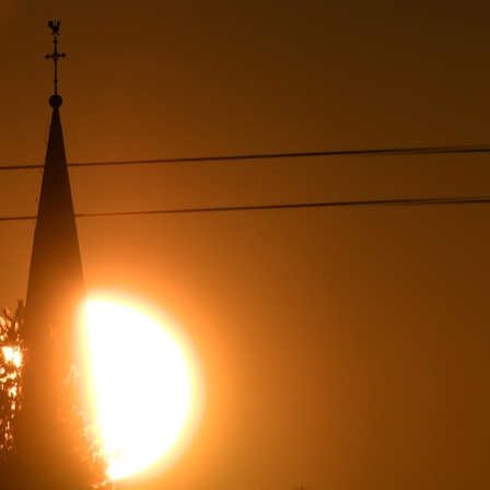 Die Sonne geht hinter der Kirche von Roggendorf bei Köln auf.