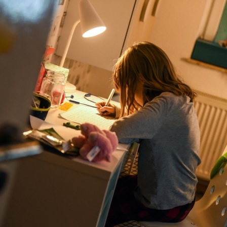 Ein Mädchen sitzt zu Hause an ihrem Schreibtisch und macht Aufgaben für die Schule.
