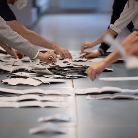 Wahlhelfer und Wahlhelferinnen zählen in einem Wahllokal Stimmzettel für die Bundestagswahl.