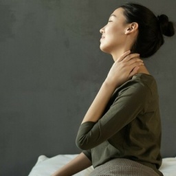 Eine Frau sitzt auf dem Bett und reibt sich den Nacken