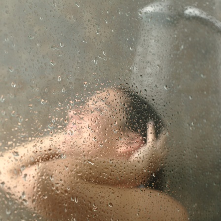 Duschen macht kreativ, sagen Forscher! Im Bild duscht eine Frau, zu sehen durch die wasserbenetzte Scheibe.