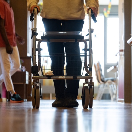 Ein Mann geht mit einem Rollator durch ein Pflegeheim.