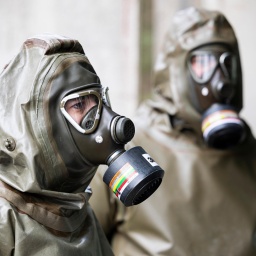 Zwei Mitarbeiter in ABC-Schutzanzügen stehen auf dem Gelände der Gesellschaft zur Entsorgung chemischer Kampfstoffe aus dem Dethlinger Teich bei Munster. 