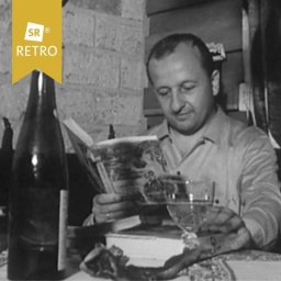 Ein Mann liest ein Buch, auf dem Tisch steht eine Weinflasche und ein Weinglas