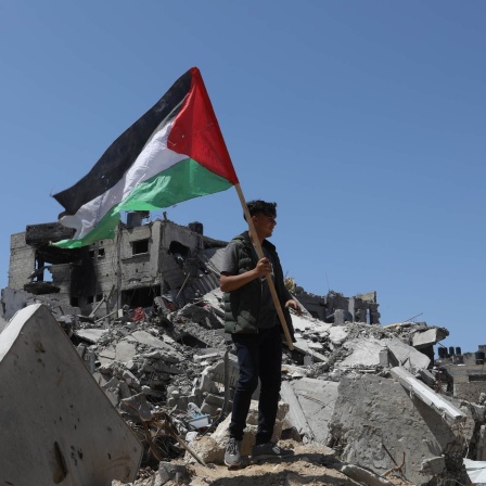 Ein Palästinenser hält die palästinensische Fahne in der Hand, während er auf Trümmern nach israelischem Beschuss stehtt.