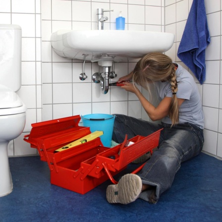 Frau repariert eine defekte Wasserarmatur in einem Badezimmer