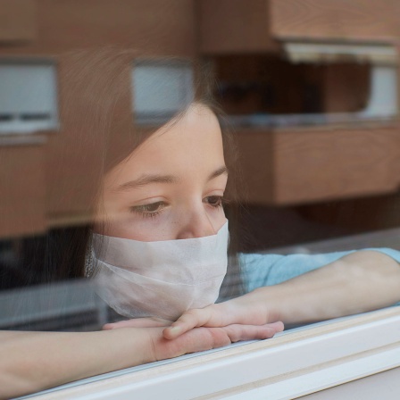 Mädchen mit Maske guckt aus dem Fenster © imago images / Cavan Images