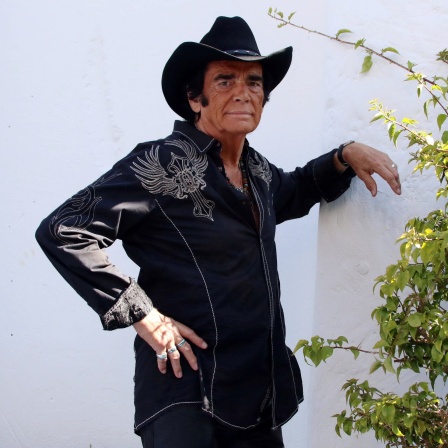 Tom Astor in Country-Outfit und Cowboyhut vor einer weißen Wand