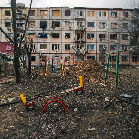 Eine Wippe steht in einen leeren Kindergarten vor einem nach russischem Beschuss völlig zerstörten Gebäude.