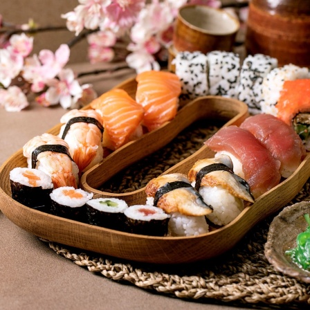 Neben einem Teller mit feinem Sushi steht ein Becher und eine kleine Schale mit Algensalat.